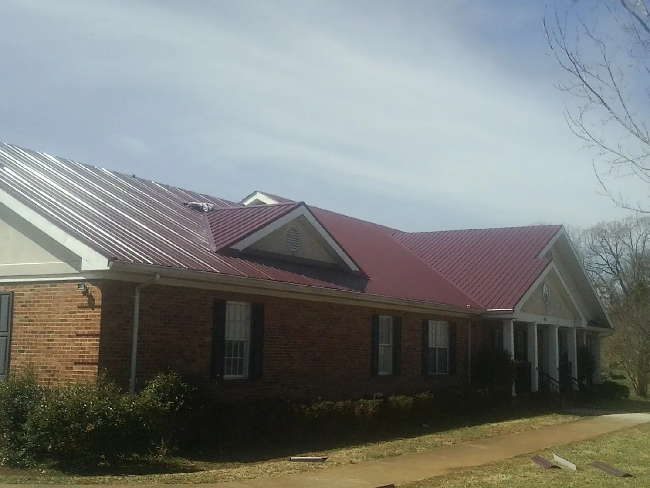 Red metal roof with gabled entries on a long brick building, from a Hail Damage Roof Repair job in Twinsburg