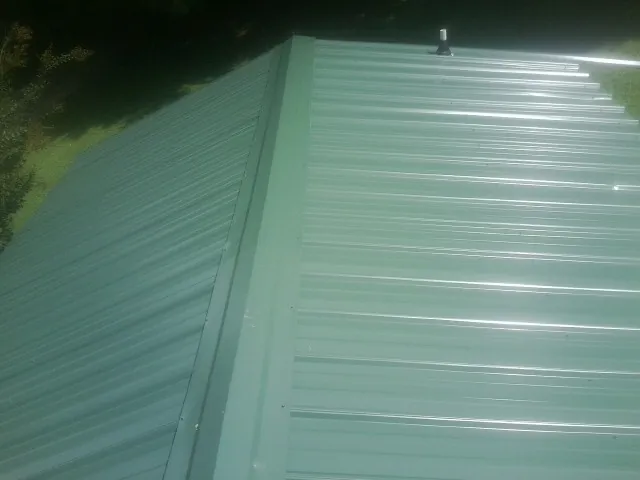 New green metal panels meeting at the ridge of a roof — Flat Roof Repair work by our crew in Twinsburg