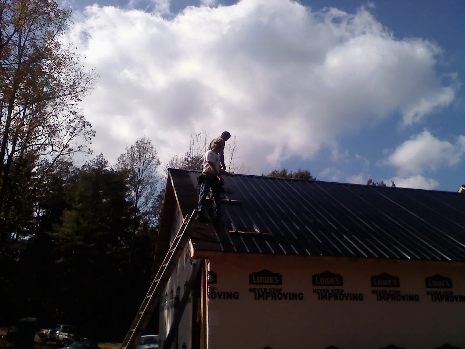 Roofer fastening dark metal panels high against a cloudy sky, from a Roof Inspection job in Twinsburg