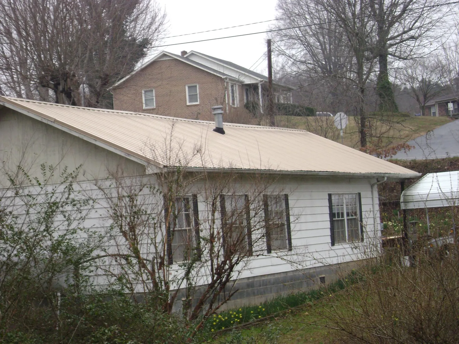 Tan metal roof on a white sided house set into a hillside — Commercial Roofing by Roofing Brothers in Twinsburg
